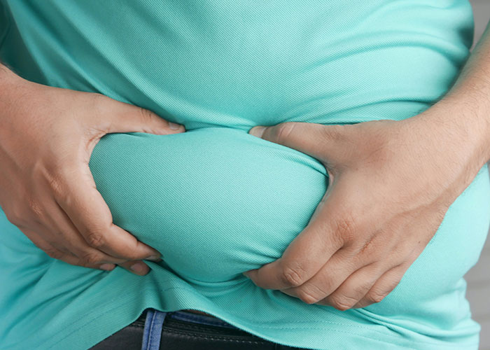 Paciente con sobrepeso agarrando su abdomen, ilustrando casos médicos donde la atención temprana es crucial según médicos.