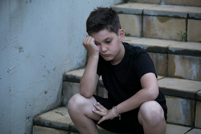 Niño triste sentado en escaleras, reflejando emociones de cosas que escuchó accidentalmente y no puede olvidar.