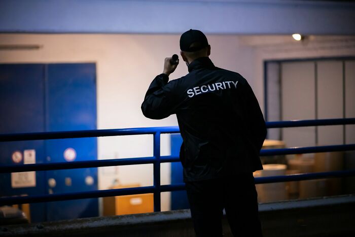 Guardia de seguridad de espaldas con linterna, en un entorno oscuro, representando cosas que escucharon accidentalmente.