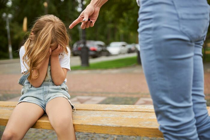 Niña triste cubriéndose el rostro mientras una persona señala y reprocha, ilustrando las peores cosas que escucharon accidentalmente.