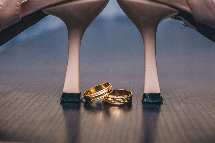 Anillo de boda dorado junto a tacones beige sobre piso de madera, representando datos sorprendentes de Hoy aprendí.