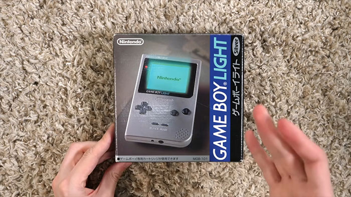 Manos sosteniendo caja de Nintendo Game Boy Light sobre alfombra, mostrando un dato sorprendente de hoy aprendí.