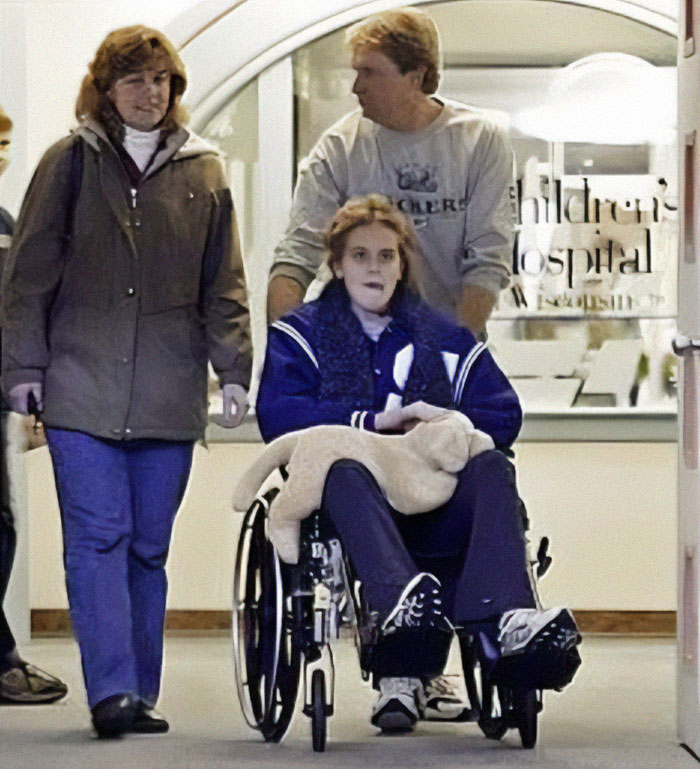 Joven en silla de ruedas saliendo de hospital, acompañada por dos personas, momento interesante que la gente comparte.