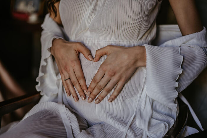Mujer embarazada en vestido blanco haciendo forma de corazón con las manos sobre su vientre, momento que cambió la historia.