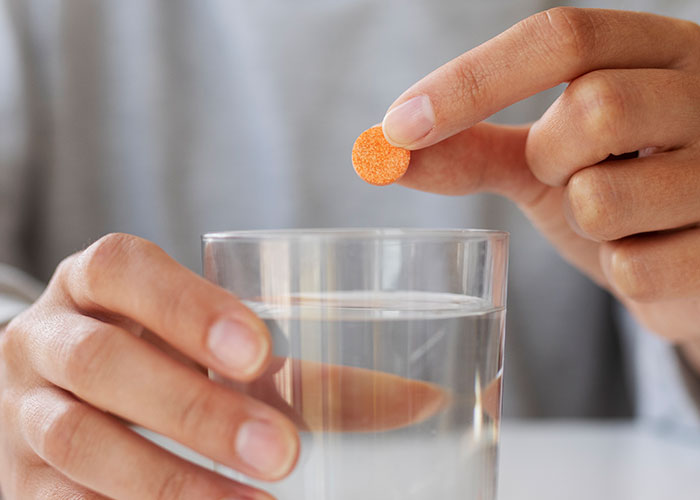 Persona con instinto de supervivencia tomando pastilla efervescente en vaso de agua transparente.