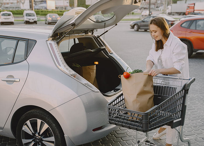 Mujer cargando bolsas de supermercado en coche, mostrando instinto de supervivencia y organización en compras.