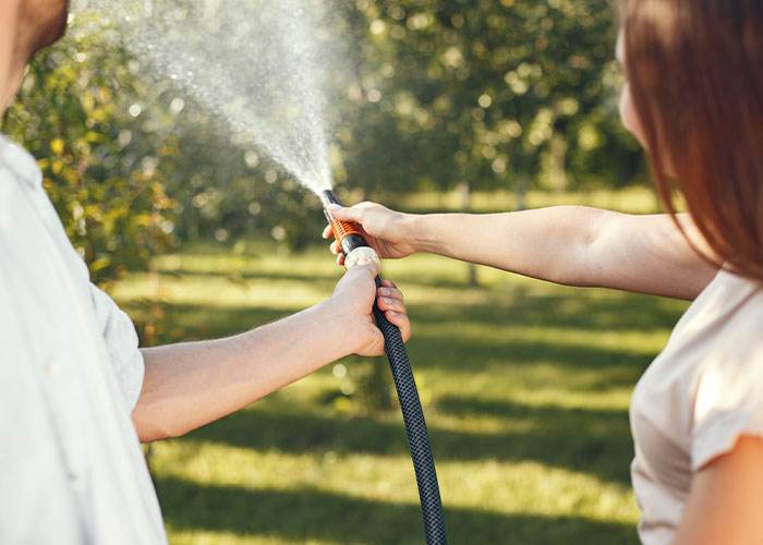 Persona con instinto de supervivencia usando una manguera para rociar agua en un jardín soleado y verde.