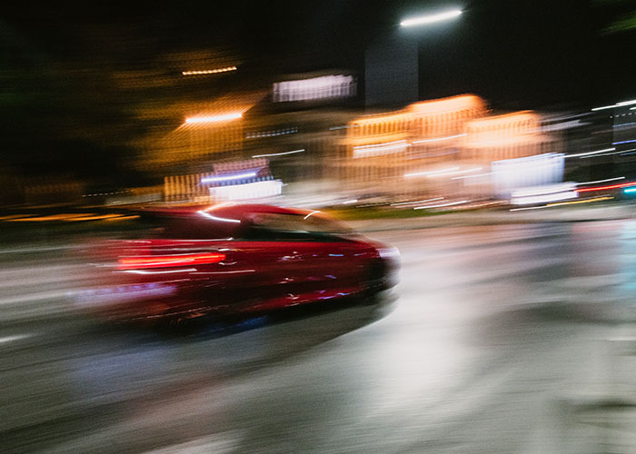 Auto rojo en movimiento rápido en calle nocturna con luces y sensación de instinto de supervivencia en acción.