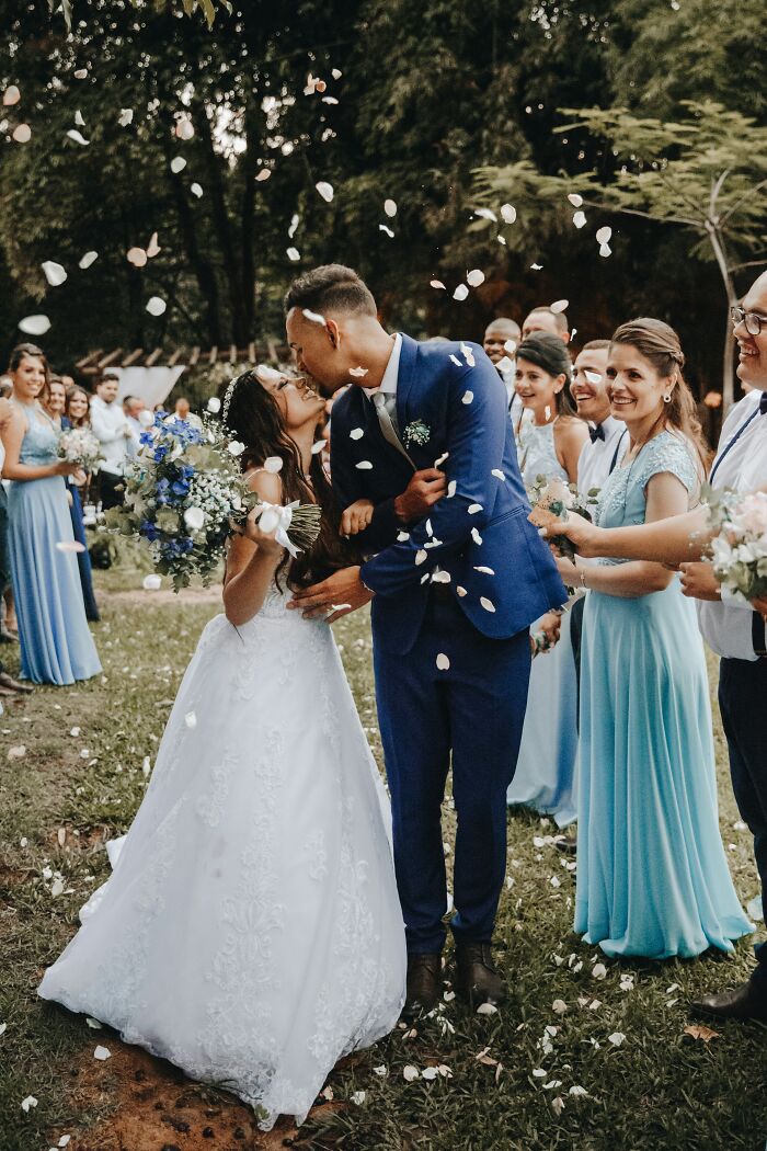 Pareja de novios besándose en boda al aire libre con petalos cayendo, celebrando momentos que ignoraron su intuición.