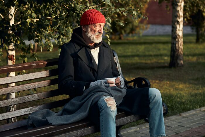 Hombre mayor en banco del parque, vistiendo gorro rojo, reflexionando sobre personas que ignoraron su intuición.