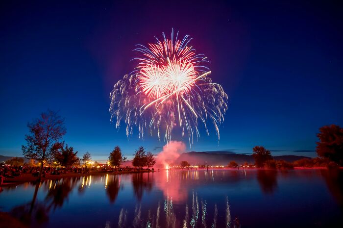 Fuegos artificiales sobre un lago al anochecer con reflejos y personas observando, intuición y decisiones acertadas.