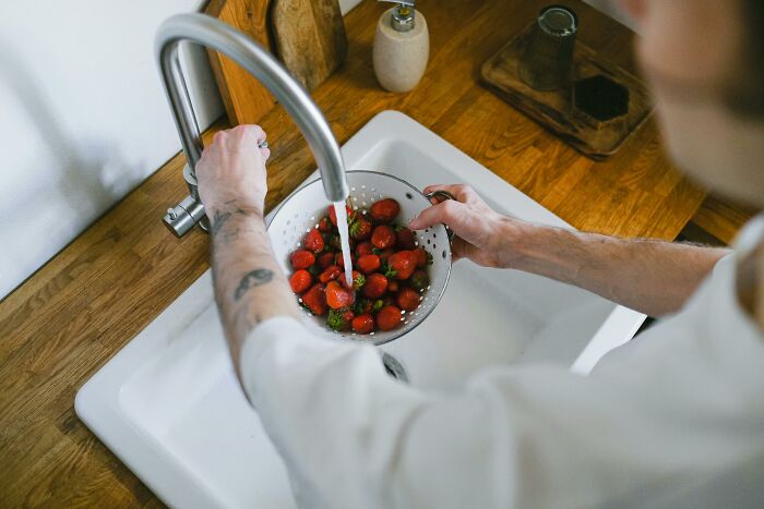 Persona lavando fresas en colador sobre fregadero, representando secretos que las empresas ocultan a sus clientes.
