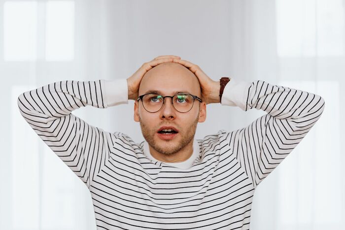 Hombre con gafas y camiseta a rayas con expresión de sorpresa tras escuchar algo que no puede olvidar accidentalmente.