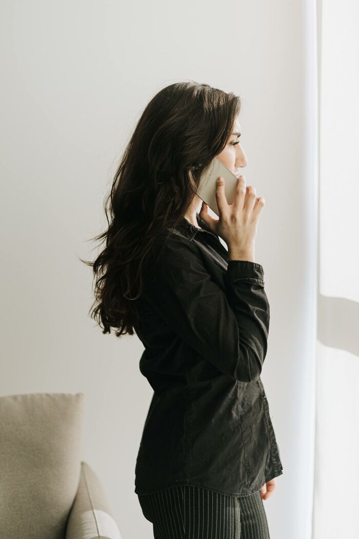 Mujer de perfil hablando por teléfono, escuchando accidentalmente cosas difíciles de olvidar en una llamada importante.