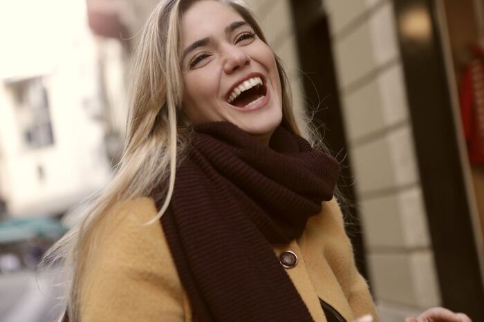 Mujer sonriente con bufanda marrón y abrigo amarillo, representando momentos que la gente no puede olvidar al escuchar cosas.
