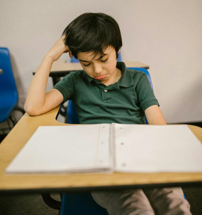 Niño en aula con expresión triste, sentado frente a cuaderno abierto, recordando cosas que escuchó accidentalmente