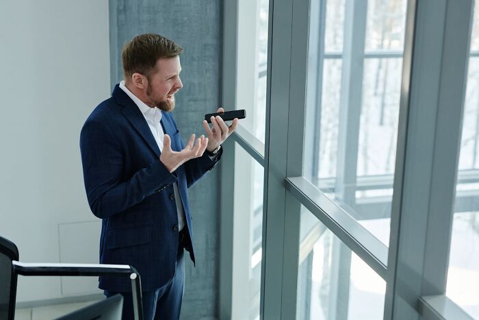 Hombre molesto hablando por teléfono cerca de ventana, representando lo peor que escucharon accidentalmente.