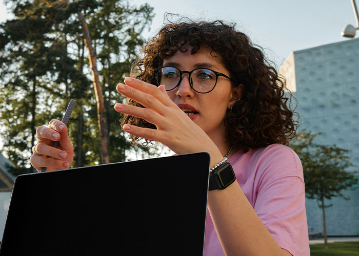 Mujer con gafas explicando algo con gesto enfocado, frente a laptop, representando investigadores privados en el trabajo.