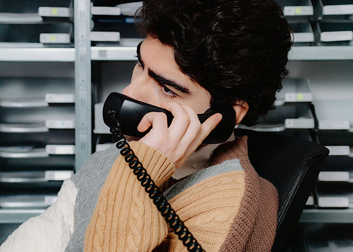 Investigador privado hablando por teléfono en oficina con estantes llenos de carpetas, trabajando en casos complejos.