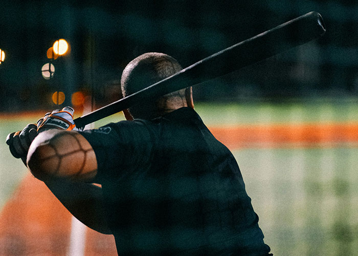 Investigador privado revisando evidencias en un campo oscuro mientras sostiene un bate de béisbol al atardecer.