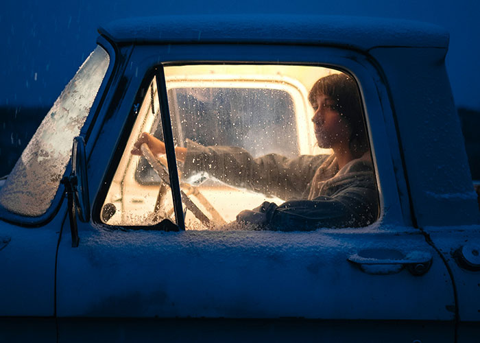 Investigador privado en coche antiguo durante noche lluviosa, representando encuentros extraños en investigaciones privadas.