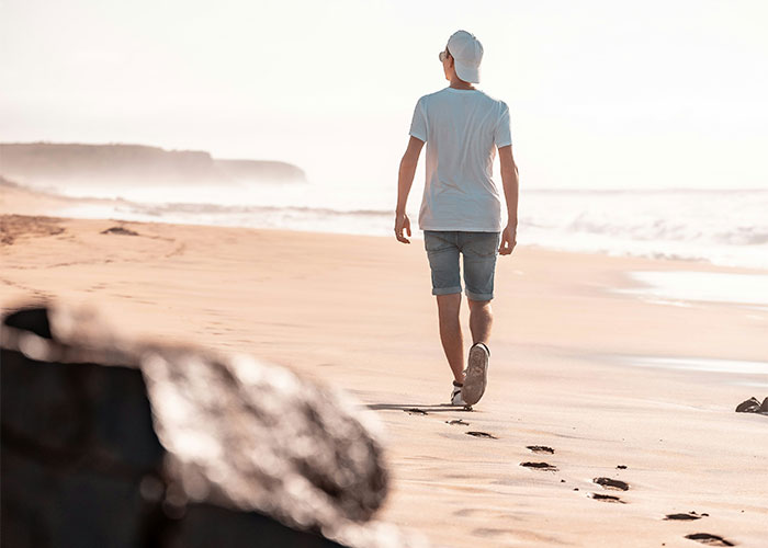 Hombre camina solo en la playa dejando huellas, representando las experiencias extrañas de investigadores privados.
