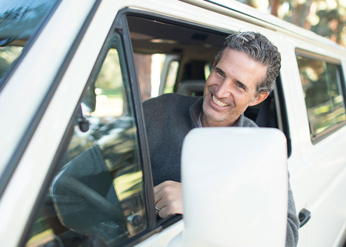 Hombre sonriente en un vehículo, representando a investigadores privados en situaciones inusuales durante su trabajo.