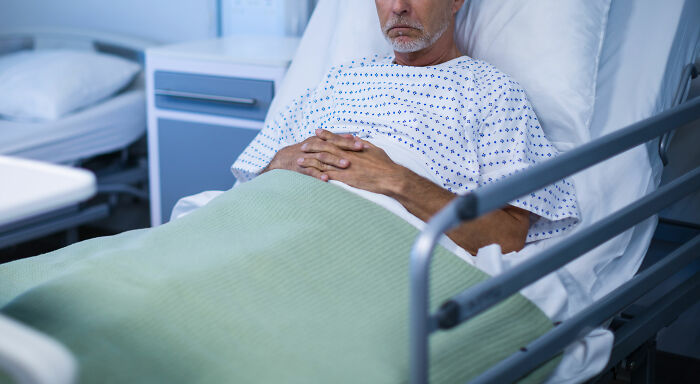 Hombre mayor en cama de hospital con expresión seria, reflejando momentos desquiciados y deprimentes en familia.