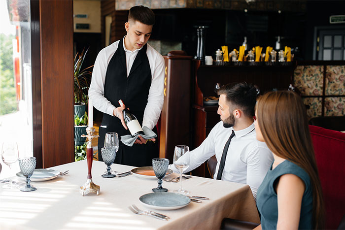 Camarero sirviendo vino a pareja en restaurante mientras observan su servicio durante una cita terrible.