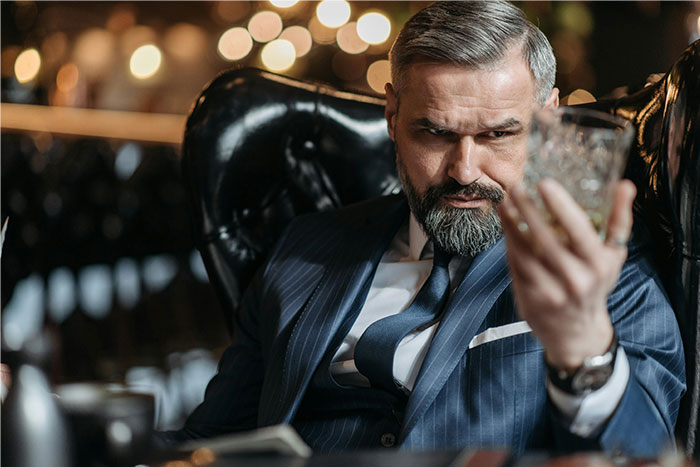 Hombre con traje azul en restaurante, sosteniendo vaso y mostrando expresión seria durante una cita terrible presenciada.