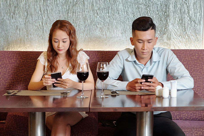 Pareja en citas terribles usando sus teléfonos en restaurante, reflejando desconexión y falta de comunicación.