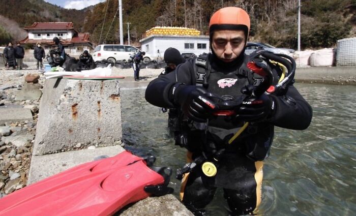 Buzo con equipo de buceo preparando inmersión en un río, mostrando datos curiosos sobre actividades acuáticas peligrosas.