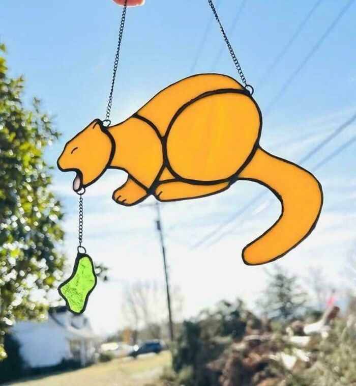 Escultura colgante creativa de un gato amarillo lamiendo un colgante verde, ejemplo de habilidades para hacer ideas malas realidad.