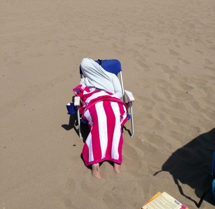Persona cubierta con toalla de rayas rosas y blancas descansando en silla de playa en divertido momento de vacaciones de verano.