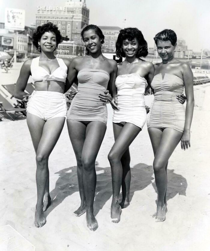 Cuatro mujeres en trajes de baño vintage sonrientes en la playa, imagen histórica fascinante para archivos visuales.