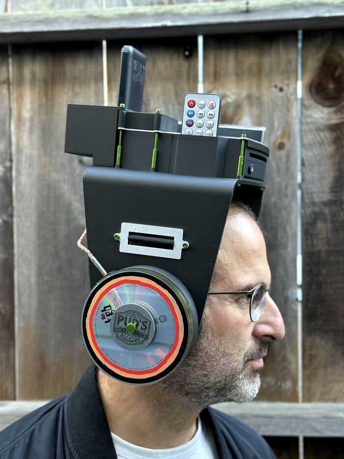 Hombre usando proyecto casero fallido con auriculares gigantes hechos de objetos reciclados y control remoto.