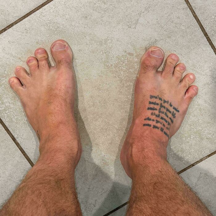 Pies con dedos y rasgos distintivos del cuerpo humano, incluyendo tatuaje en el pie derecho sobre piso de baldosas.