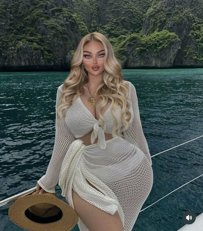 Mujer con larga cabellera rubia en traje de malla blanca posando en barco frente a paisaje natural, momentos Instagram colapsó realidad.