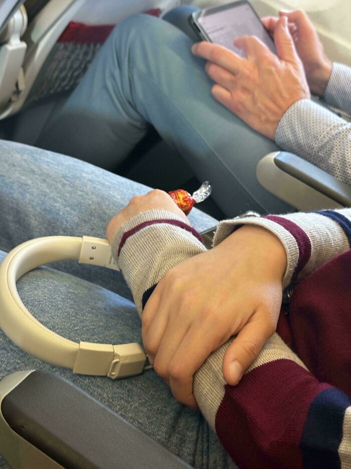 Manos de personas prepotentes en avión, una sosteniendo un dulce y otra un dispositivo electrónico.