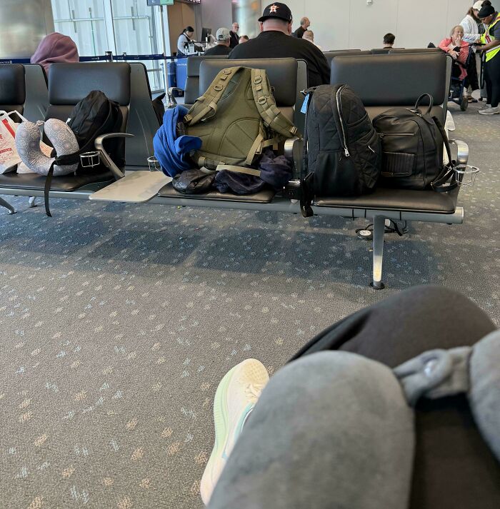 Mochilas ocupando varios asientos en sala de espera de aeropuerto, muestra personas prepotentes actuando con derecho.
