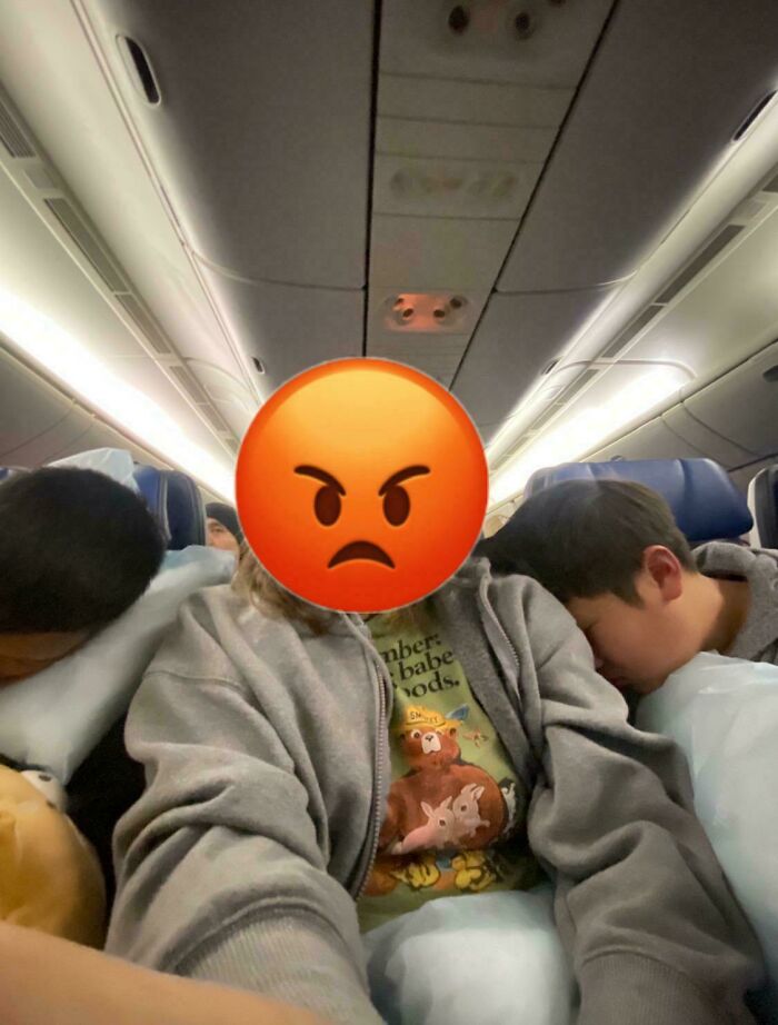 Persona prepotente con emoji en cara, sentada en avión entre dos pasajeros dormidos, imagen de comportamiento arrogante.