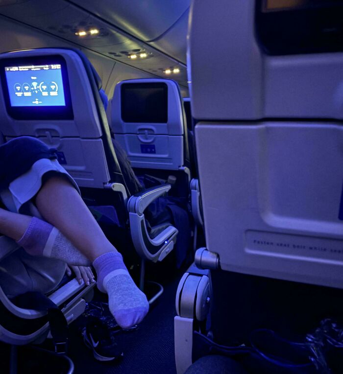 Pasajero con actitud prepotente en avión, con los pies sobre el asiento delantero, causando incomodidad a otros viajeros.