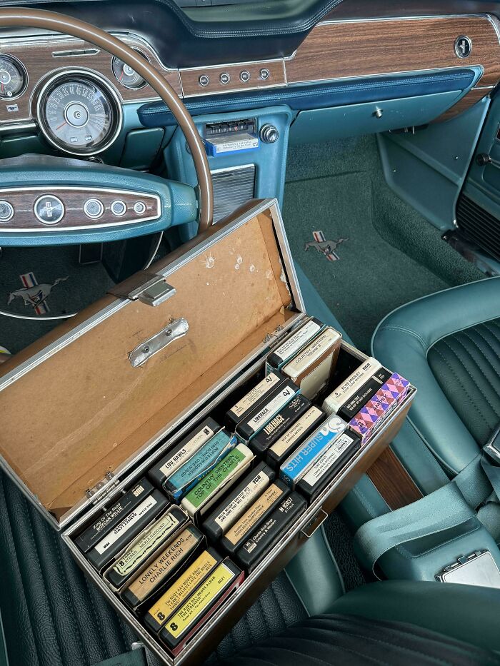 Interior de coche clásico con maletín abierto lleno de cintas de casete, mostrando objetos que ya no existen hoy.