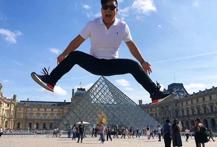 Hombre divertido saltando frente a la pirámide del Louvre en vacaciones de verano, captura de momento divertido para compartir.