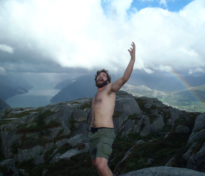 Hombre sin camiseta en la montaña disfrutando y celebrando durante las vacaciones de verano con un arcoíris de fondo.