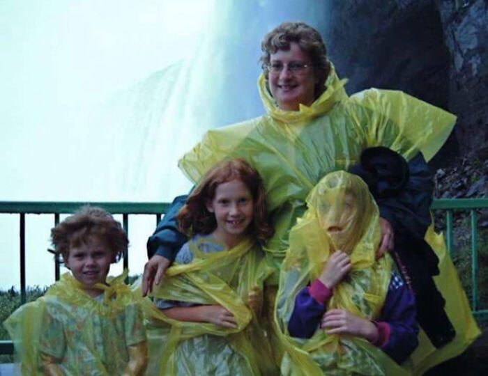Familia con ponchos amarillos disfrutando de divertidas fotos de las vacaciones de verano junto a una cascada.