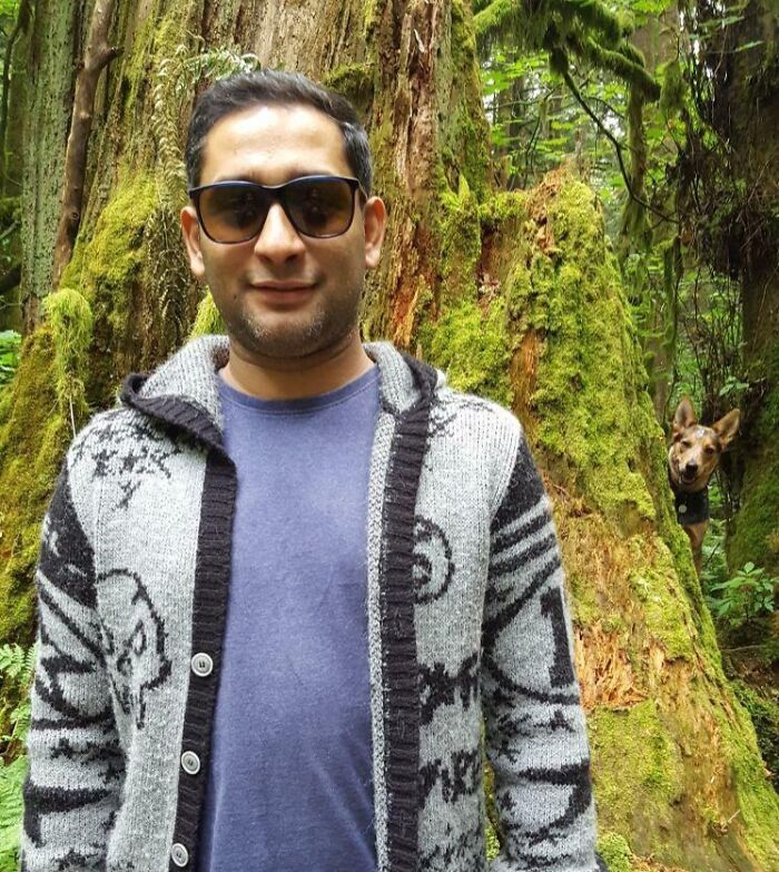 Hombre con gafas de sol en el bosque mientras su mascota aparece divertida arruinando la toma perfecta en la naturaleza.