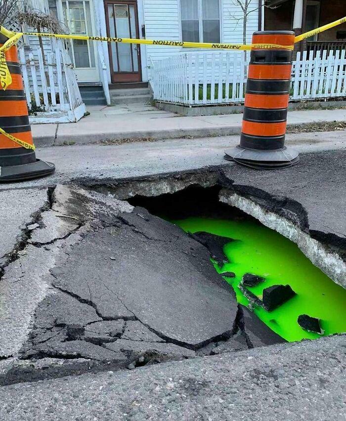 Enorme agujero en la calle con líquido verde brillante, causando una escena aterradora y espeluznante en zona residencial.
