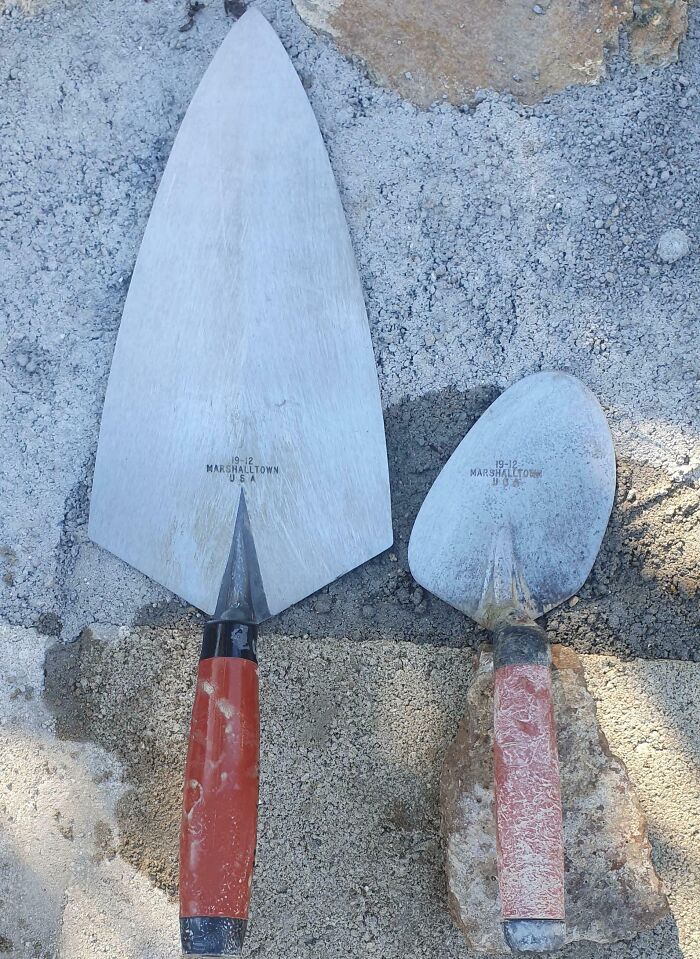 Dos paletas de albañil de diferente tamaño sobre superficie de cemento mostrando comparaciones y diversidad inesperada de la vida.