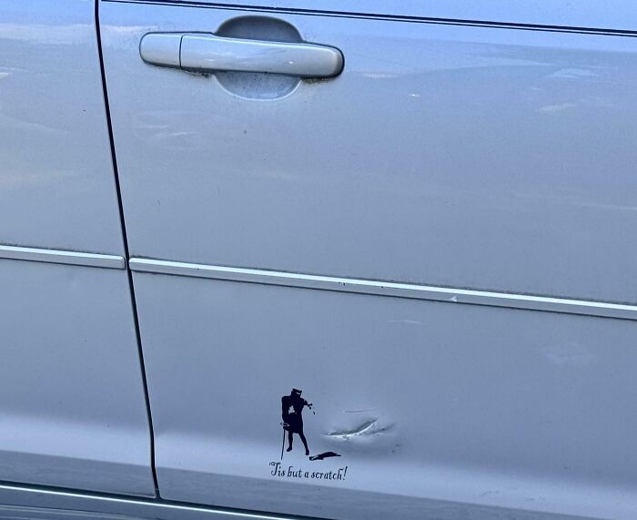 Dibujo humorístico en puerta de coche con abolladura, mostrando el ingenio y humor ingenioso de las personas.